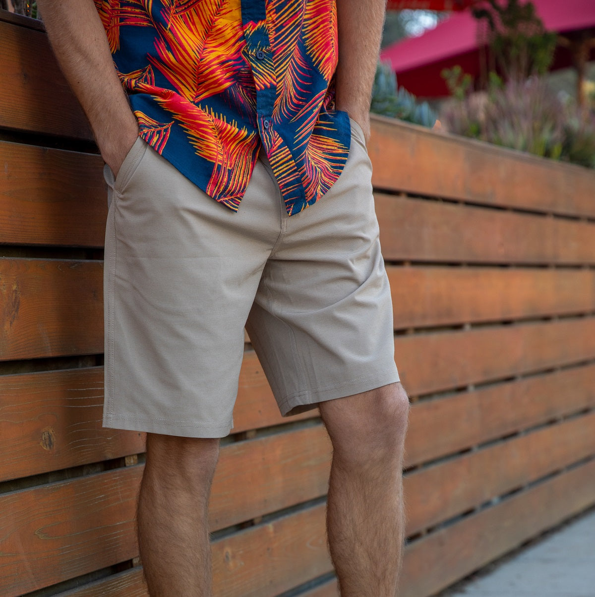 Men wearing beige Dante Walk Short standing against a wooden fence, beach-inspired casual apparel for everyday comfort.
