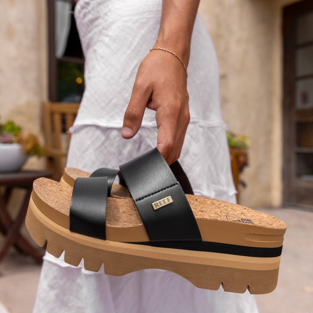 Woman holding Cushion Vista Higher sandal facing right showing black straps and thick cushioned sole with anatomical arch support