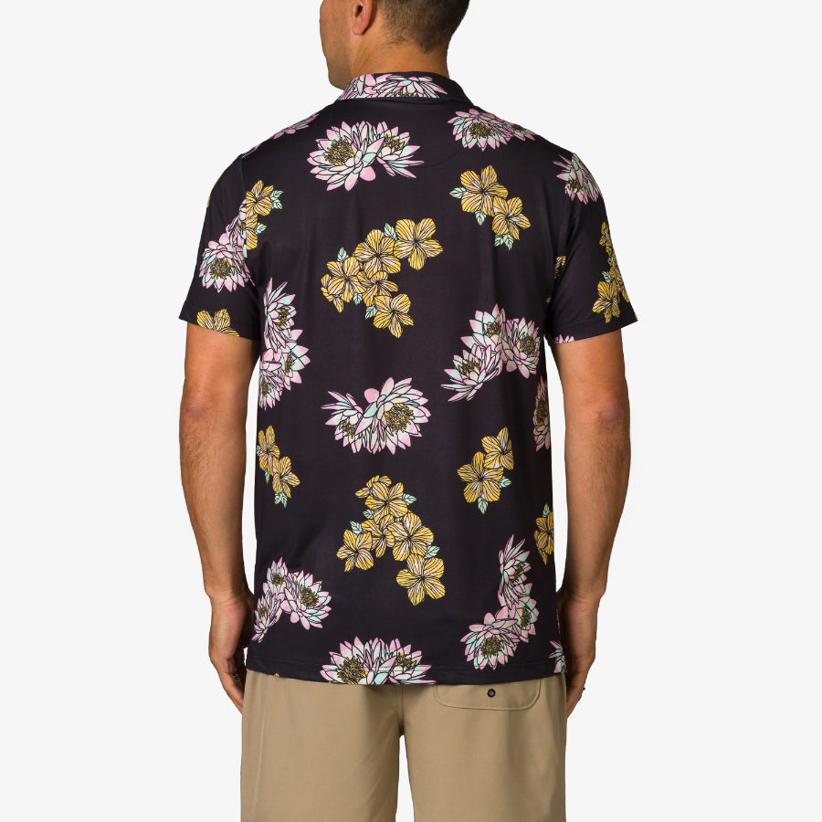 Man wearing Wesland Polo shirt facing away, black with yellow and white floral print, casual beach-inspired style