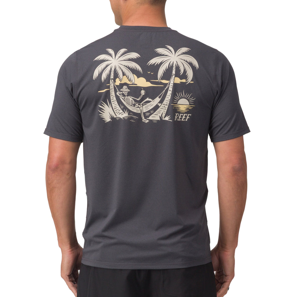Back view of a man wearing the dark gray Siesta Performance Shirt with a beach hammock graphic and palm trees.