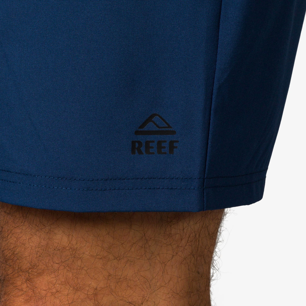 Close-up of the lower leg wearing navy blue Garland Hybrid Short showing the REEF logo, beach-inspired comfort apparel.