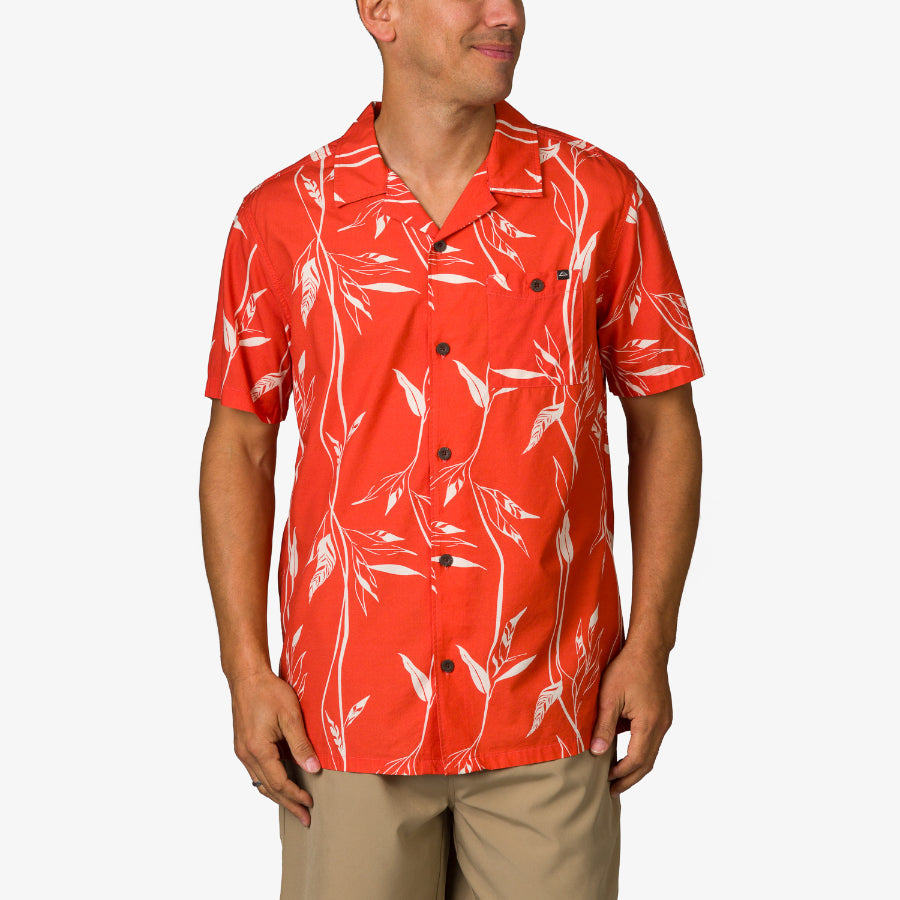Man wearing a red Kaden Camp Shirt with white leaf pattern, front view showing buttons and short sleeves, beach-inspired apparel.