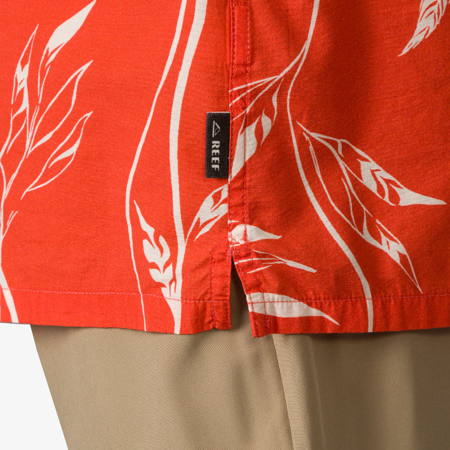 Close-up of the hem and side seam of the Kaden Camp Shirt in orange with white leaf prints, showing REEF tag.