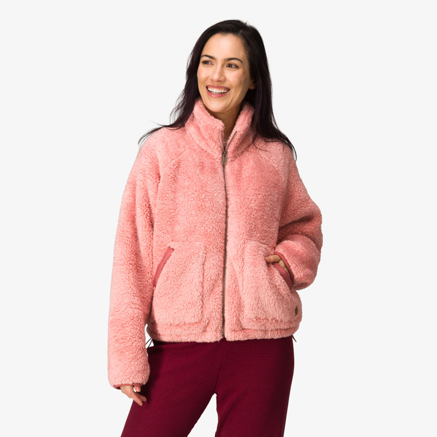 Woman wearing a pink Pilot Sherpa Jacket facing front with hands in pockets, showcasing comfort and cozy beach-inspired apparel.