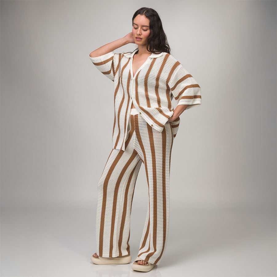 Woman wearing Mika Sweater Pant in brown and white stripes, standing with one hand behind head, front view, barefoot.