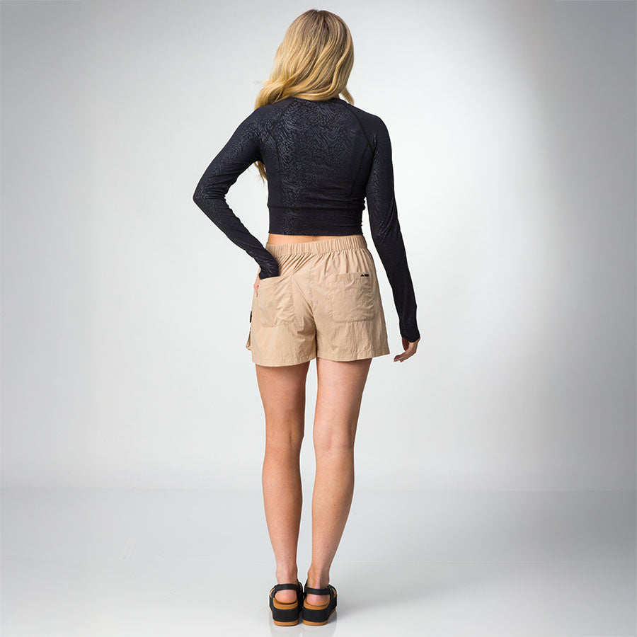 Woman wearing the Flex Performance Shirt in black, showing back view with long sleeves and thumb holes, paired with shorts and sandals facing back.
