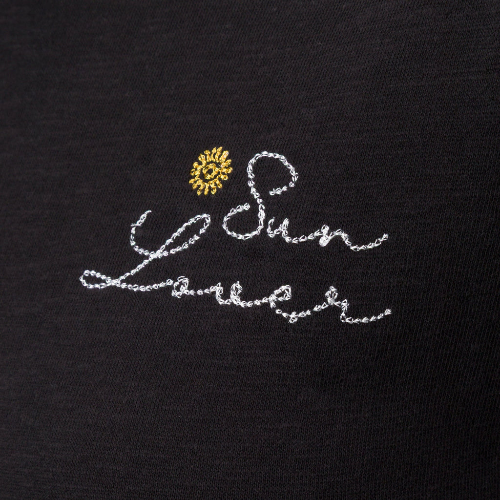 Close-up of embroidered "Sun Lover" text with yellow sun detail on black fabric of the Sun Lover Ringer Tee for women.