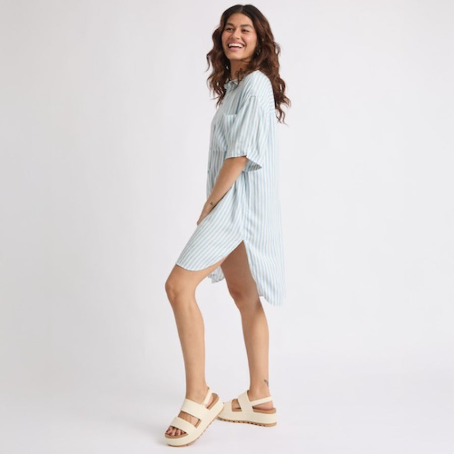 Woman wearing the Ollie Striped Shirt Dress in light blue with beige platform sandals facing left, smiling, casual beach style.