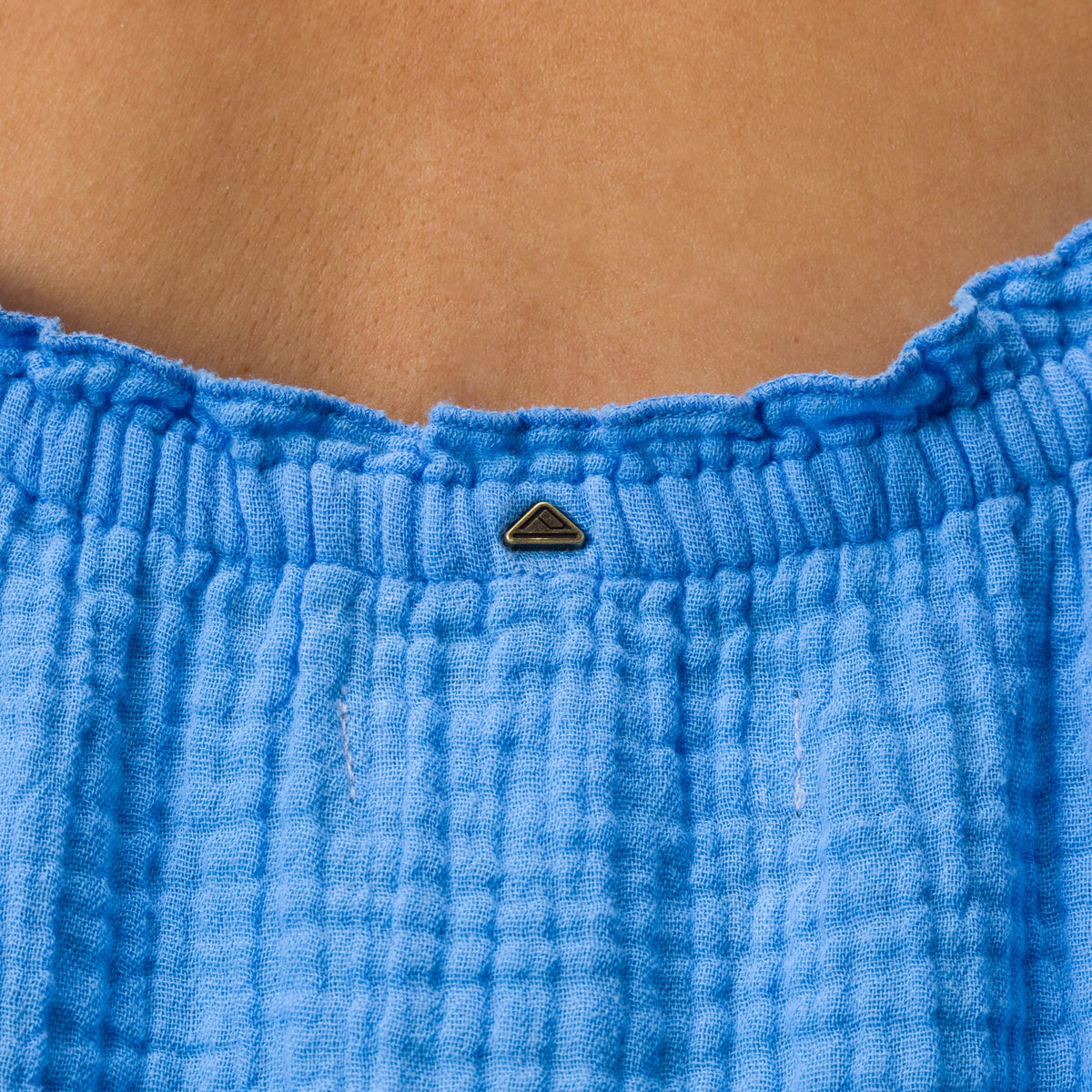 Close-up of the top back of the Lainey Maxi Dress in soft blue fabric with a small metal logo detail.