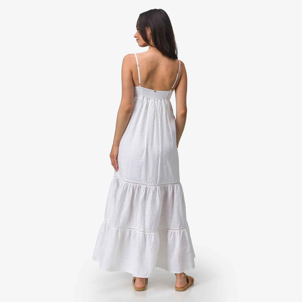 Woman wearing a white Yuni Maxi Dress facing backward, showing the dress's tiered design and adjustable straps.