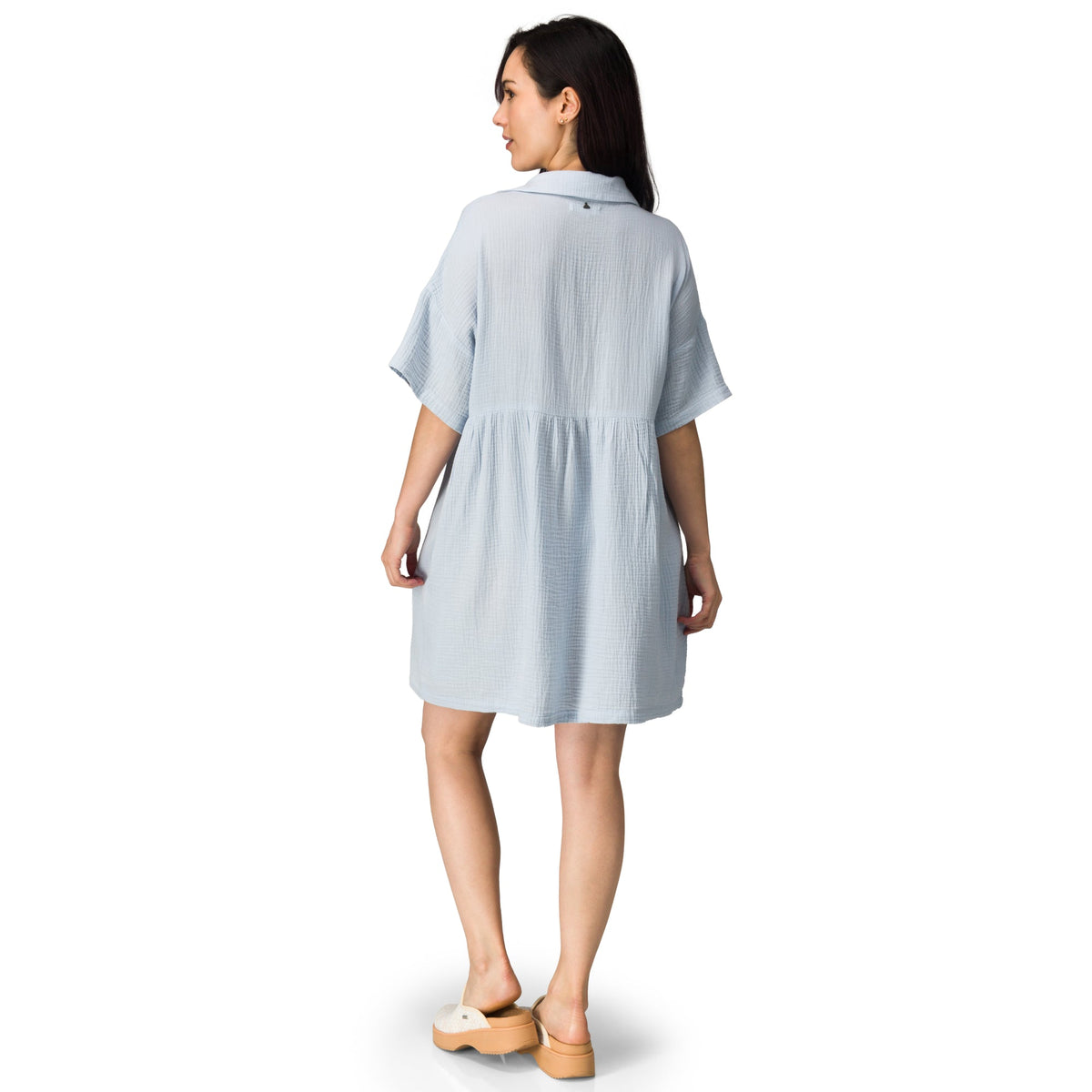 Woman wearing a light blue Lainey Shirt Dress seen from the back, paired with beige platform sandals facing right.