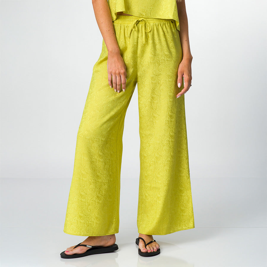 Woman wearing bright green Ollie Pant with loose fit, shown front view from waist to feet in black flip flops facing forward.