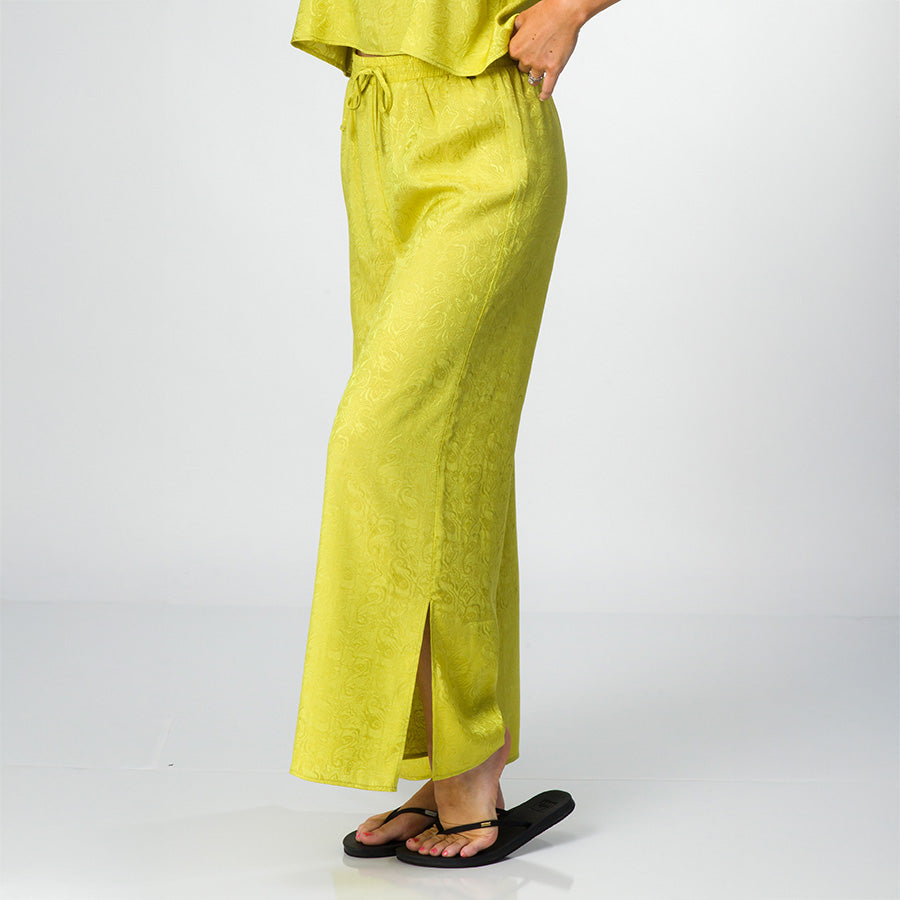 Side view of Ollie Pant in lime green with slit hem, paired with black REEF sandals facing forward for beach comfort.