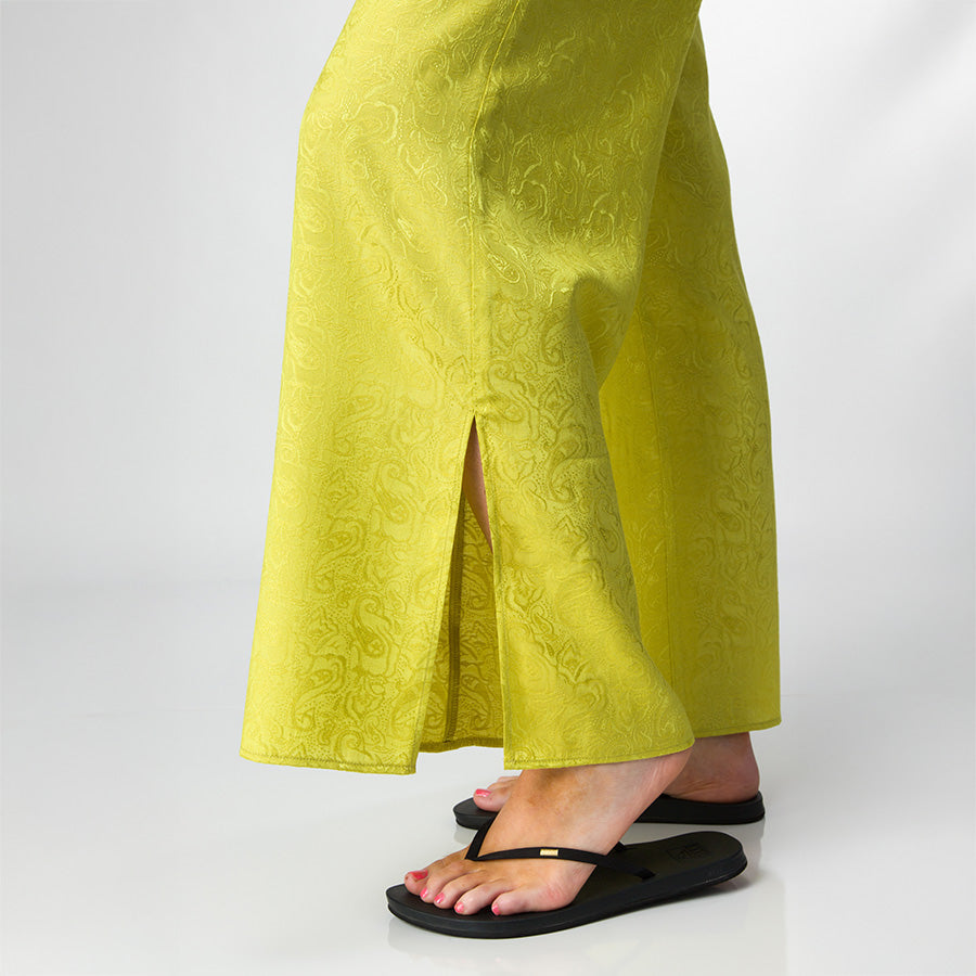 Close-up of the lower legs wearing Ollie Pant in bright yellow with print, facing right, paired with black sandals.