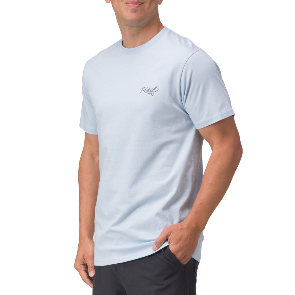 Man wearing light blue Marlinrita Tee standing with right hand in pocket, showcasing comfortable, beach-inspired apparel.