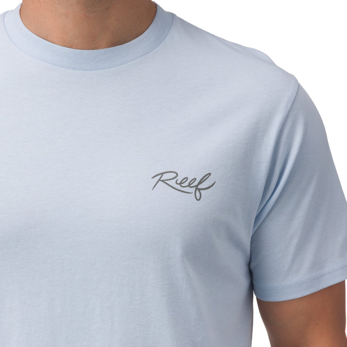 Close-up of the chest area of the Marlinrita Tee in light blue with Reef logo, men's beach-inspired comfortable apparel.