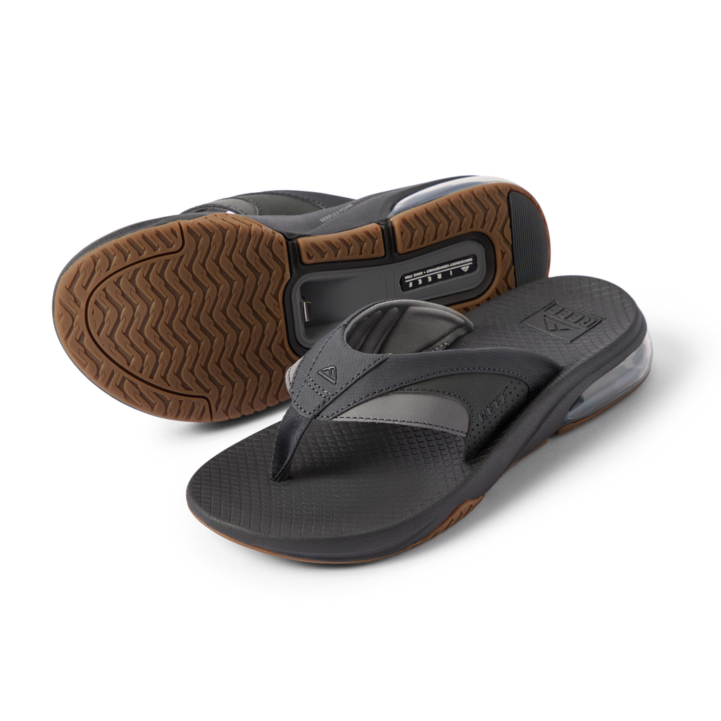 Pair of Fanning + men's black and gum flip flops, showing top view of right and sole of left, with cushioning and arch support.