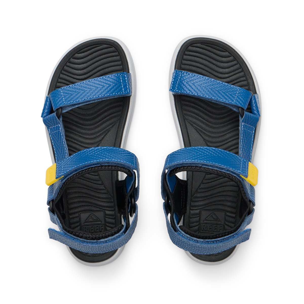Kids Shoremazing sandals facing upward, blue straps with yellow details, black textured footbeds, beach-inspired comfort design.