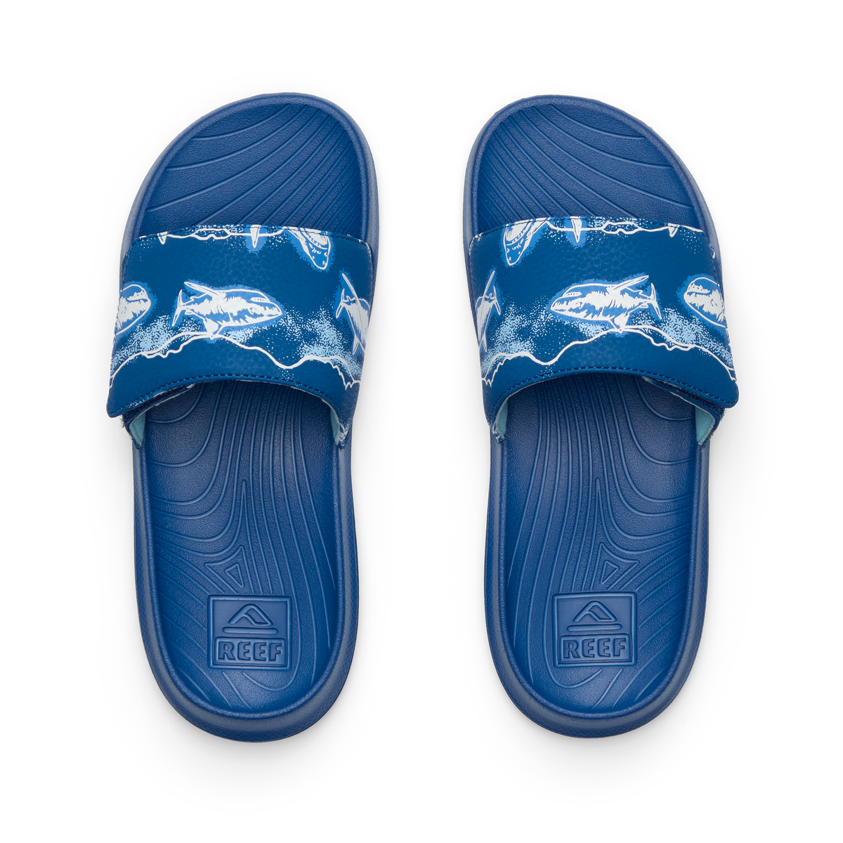 Top view of blue Kids Salty Slide facing up, featuring reef anatomical arch support and shark print strap for beach comfort.