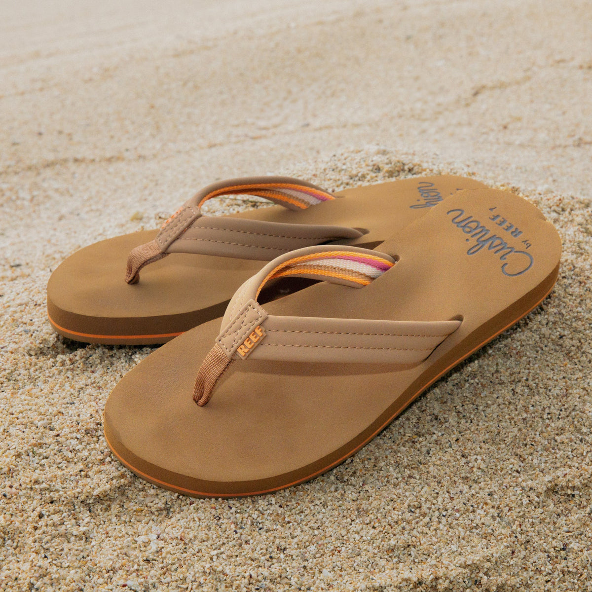 Reef Cushion Breeze sandals facing right, close-up of cushioned tan straps and supportive molded footbeds on sand.