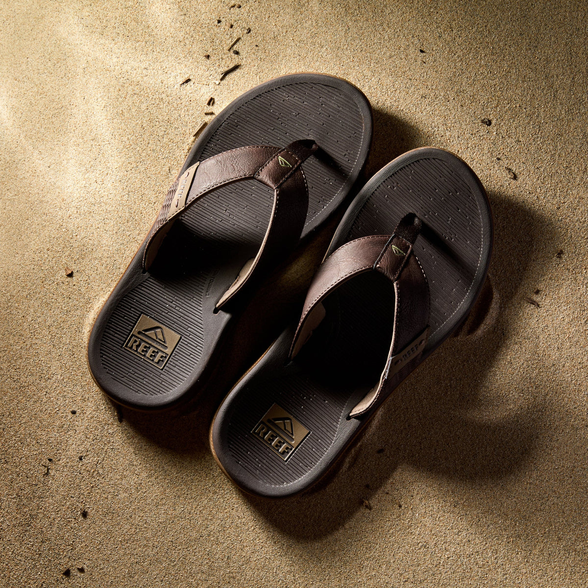 Reef Santa Ana men's sandals in brown facing upward, showcasing cushioned footbed and arch support on sand.