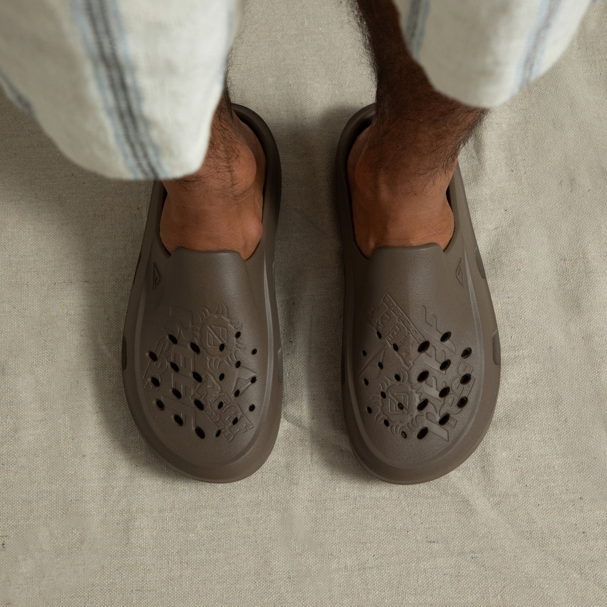 Top-down view of feet wearing brown Glider slides facing forward, showcasing water-friendly perforated toes and seamless comfort design.