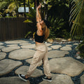Woman in black crop top and black right-facing sneakers wearing beige Cargo Jogger Pant stretching outdoors on stone path