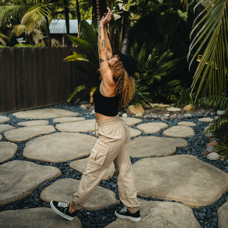 Woman in black crop top and black right-facing sneakers wearing beige Cargo Jogger Pant stretching outdoors on stone path