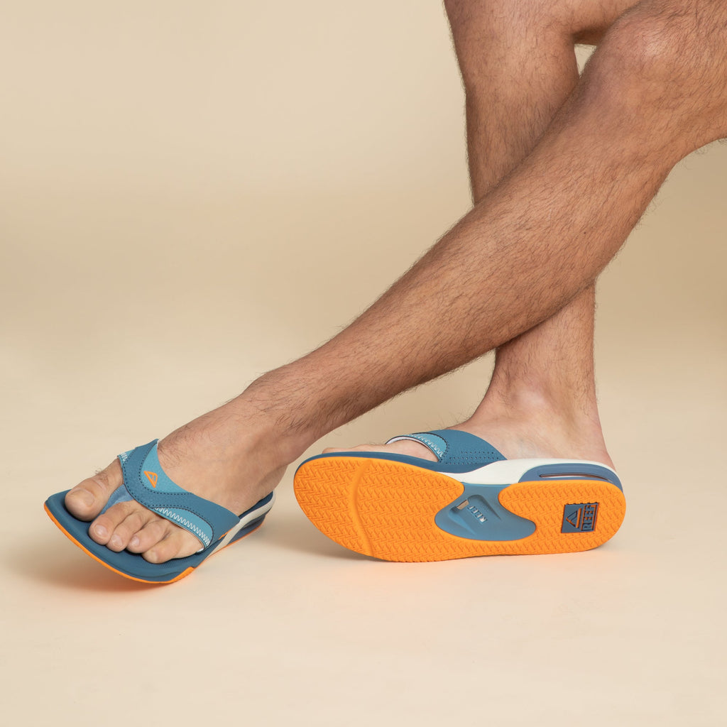 Fanning men's blue and marigold sandals, left shoe facing forward, right shoe sole up showing soft cushioning and arch support