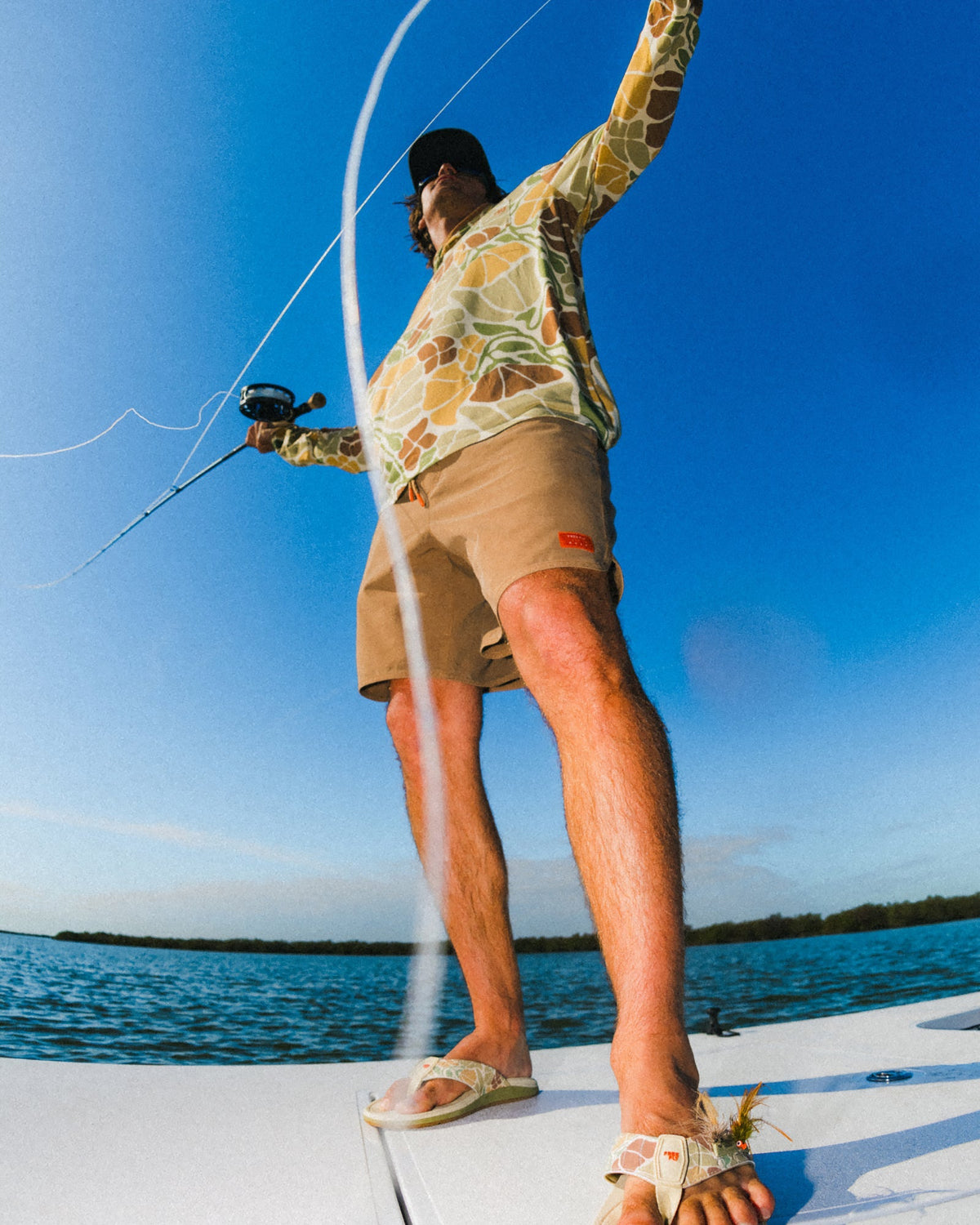 Man wearing Men's Reverb Short Unlined – 7" - Coconut facing forward standing on boat deck casting fishing line in bright sunlight