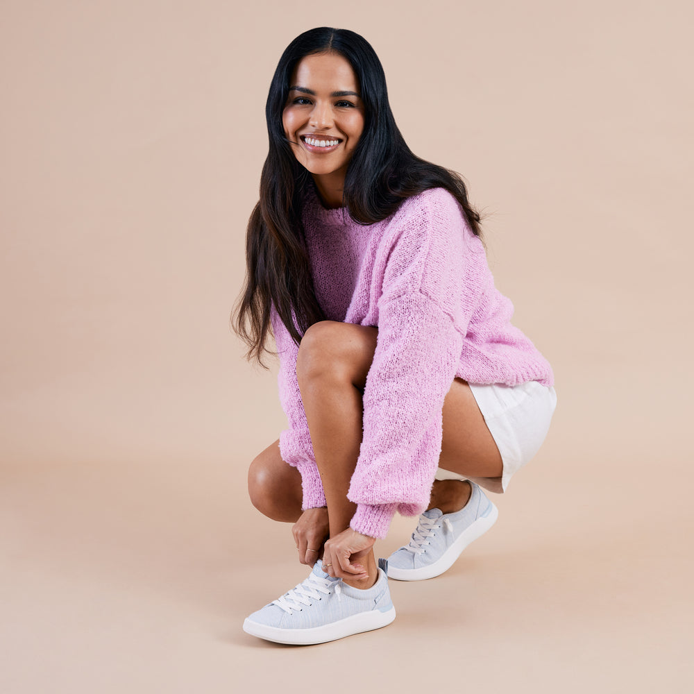 Woman crouching while wearing Neptune Alana sneakers facing left, showing side and top with soft-rebound cushioning.