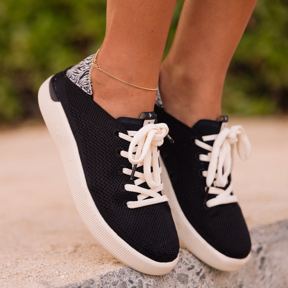 Reef Neptune women's black sneaker facing forward with white laces and zebra print heel, highlighting comfort and beach style.