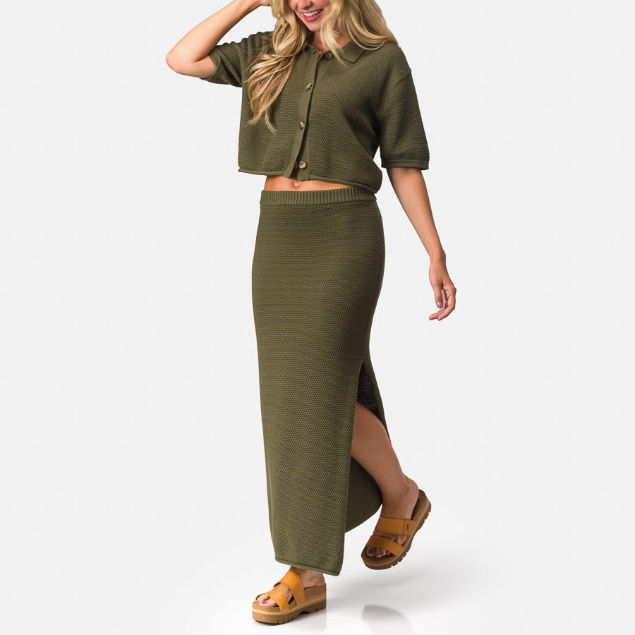Woman wearing olive green Up North Sweater Skirt with side slit, paired with tan platform sandals facing right side.