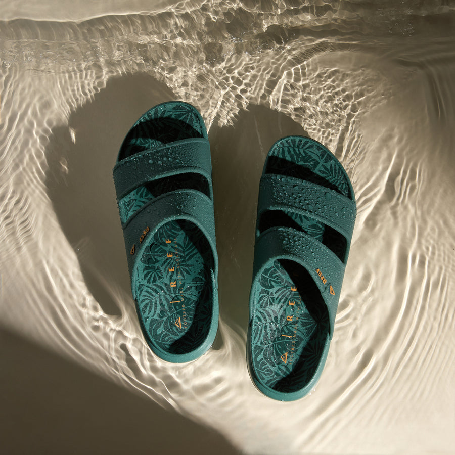 Oasis Double Up men's sandals facing up with leaf print footbeds and water droplets, designed for beach comfort.
