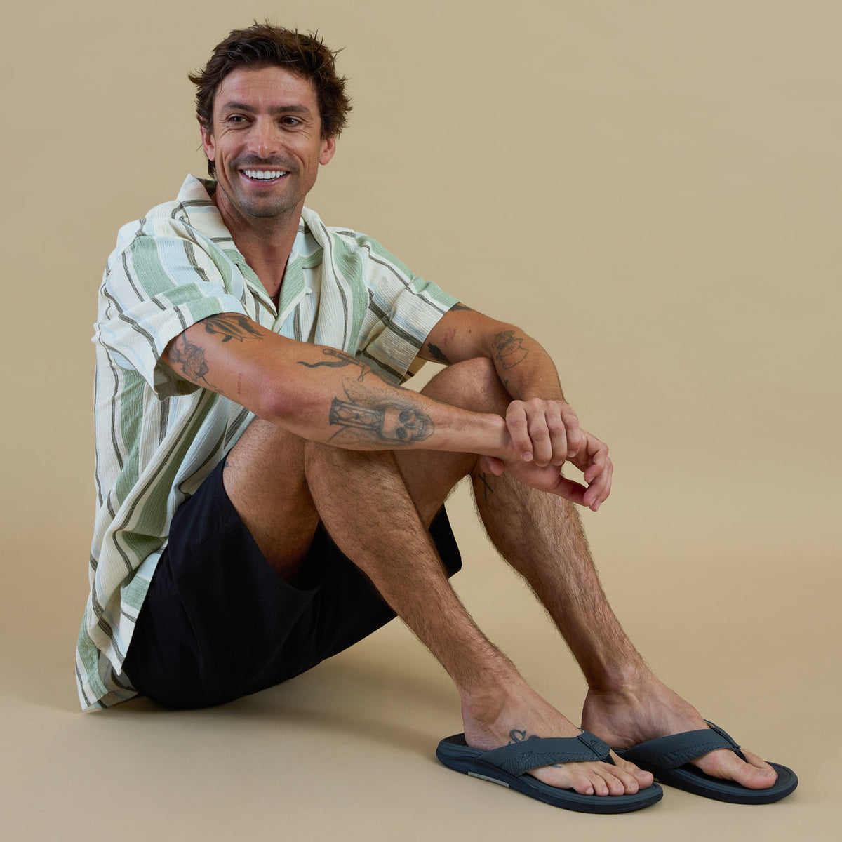 Man wearing Offshore sandals facing forward, sitting relaxed, showcasing surf-inspired comfort and beach-ready design.