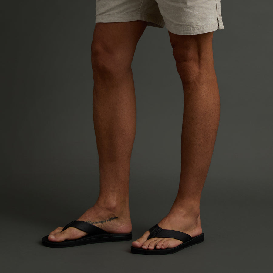 Ojai Classic black men's flip flops facing right on feet, showing lightweight, comfortable beach-inspired footwear design.