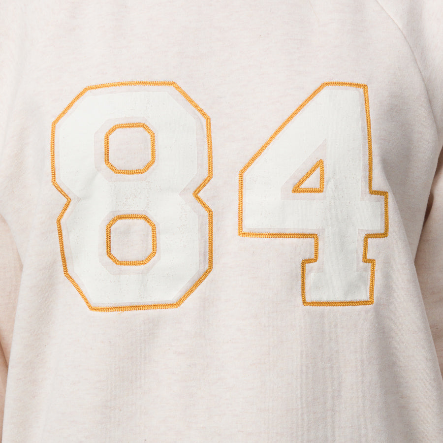 Close-up of the chest area of the women’s Oversized Raglan Fleece in oatmeal heather with embroidered number 84 detail.