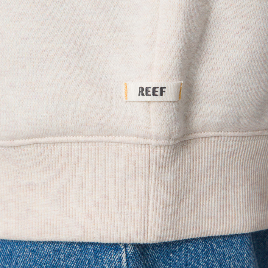 Close-up of the bottom hem on the Oversized Raglan Fleece in oatmeal heather, showing soft fabric and REEF label.