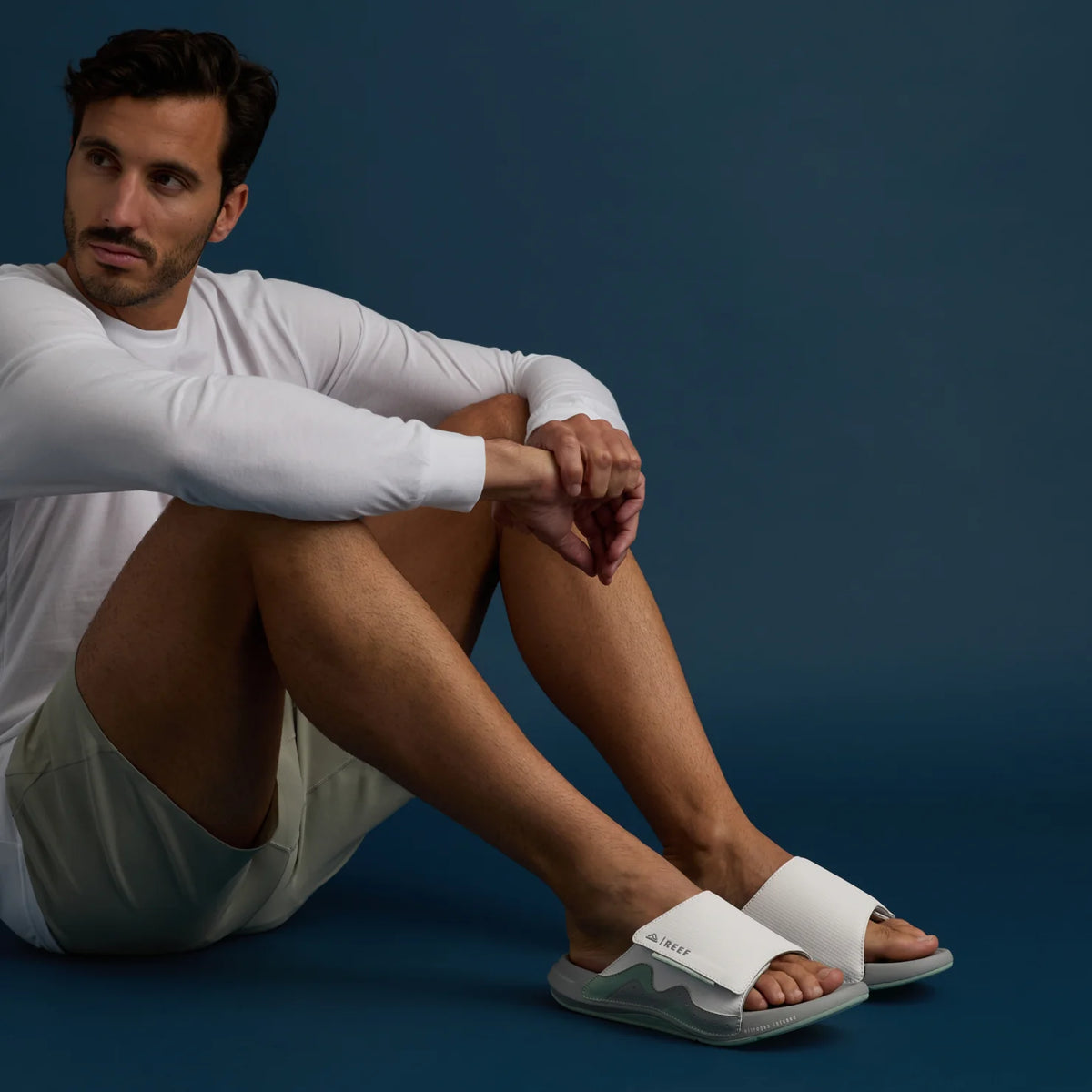 Man sitting wearing white Cruiser Slide sandals facing forward with arch support and cushioned footbed