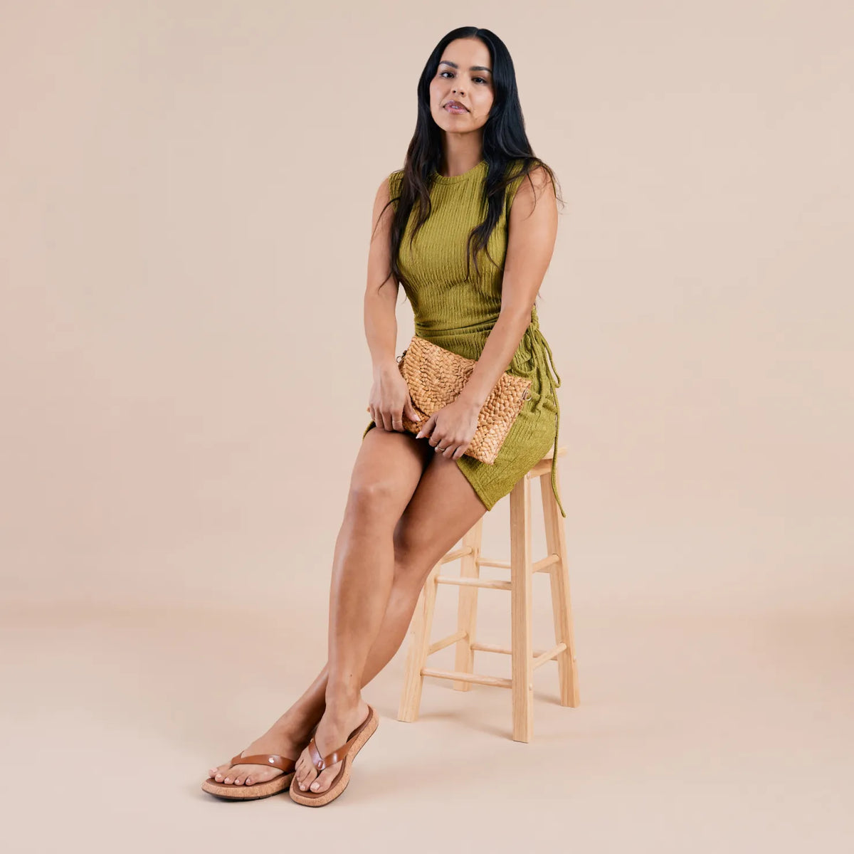 Woman seated on wooden stool wearing Sunset Low Maya tan sandals facing forward with soft-rebound cushioning and arch support