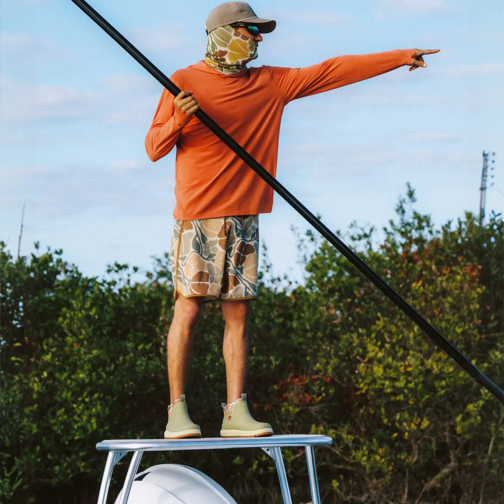 Man wearing Free Fly X Scallywag boots facing forward standing on boat platform, pointing with paddle in hand outdoors