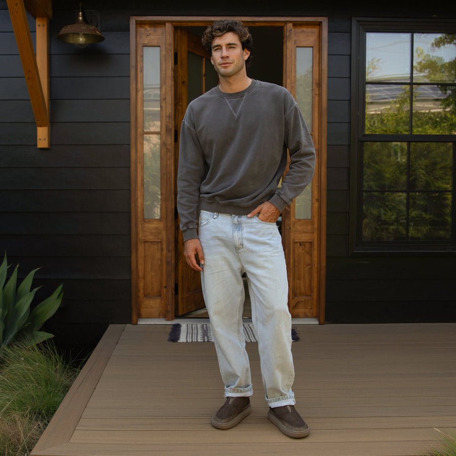 Man wearing brown Rambler Hi shoes facing forward, standing on a deck in casual beach-inspired apparel.
