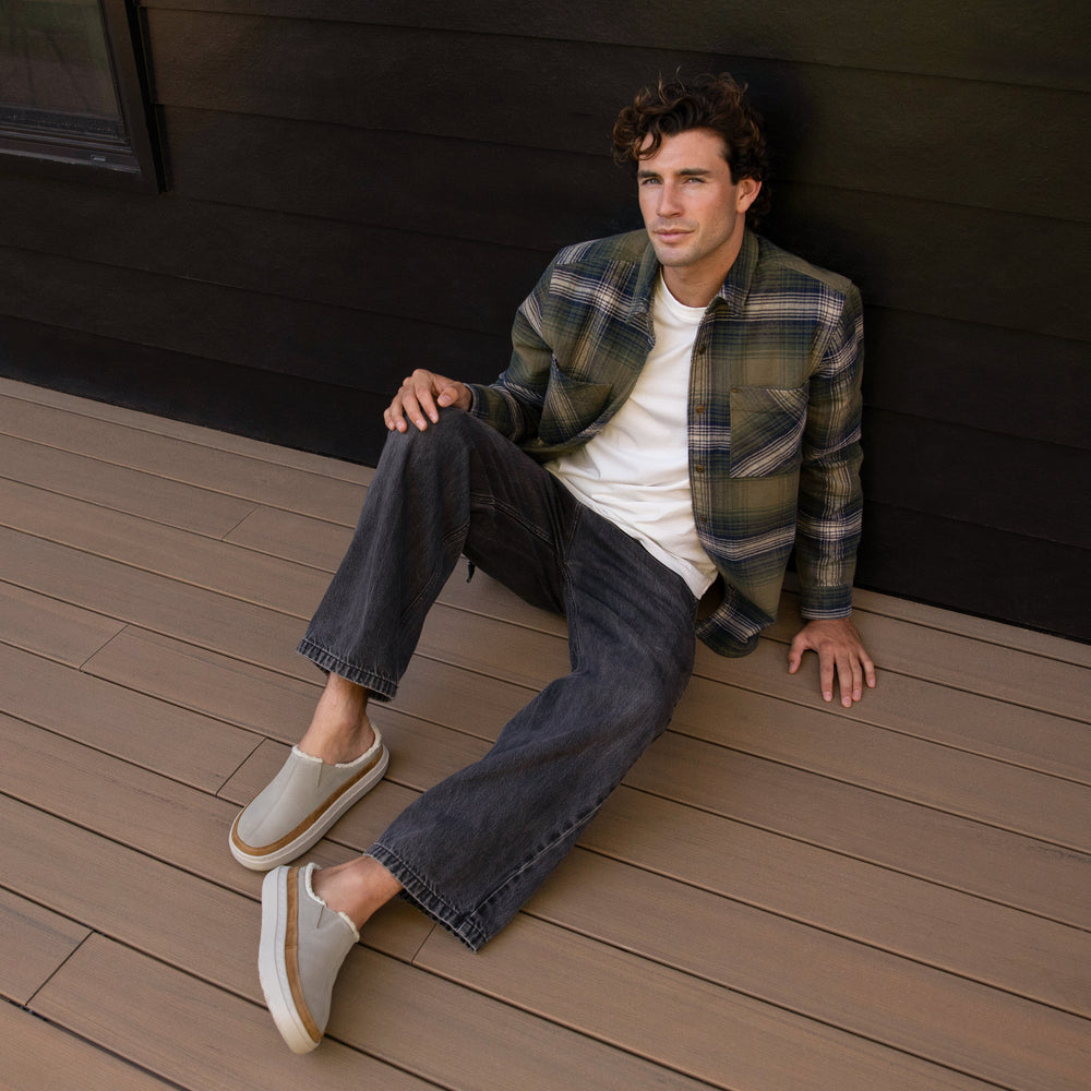 man wearing Rambler Mule Brown and jeans and a flannel sitting outside a cabin