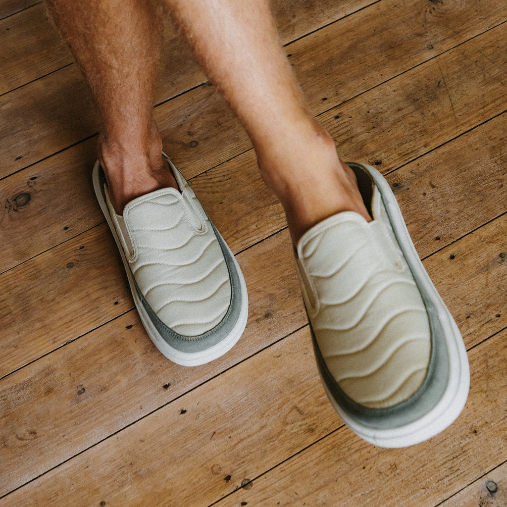 Rambler Kicker cream slip on mules facing toward the lower right on a wood floor