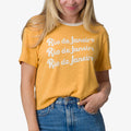 Woman wearing a honey gold Ringer Tee with white collar and Rio de Janeiro text, front view, casual beach-inspired apparel.