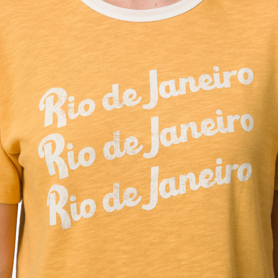 Close-up of the chest area of a women's Ringer Tee in honey gold with white trim and Rio de Janeiro text for beachwear comfort.