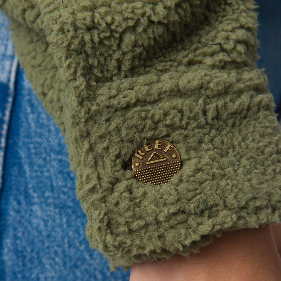 Close-up of the cuff on the Sammie Sherpa Jacket in olivine color showing textured fleece and REEF logo button.