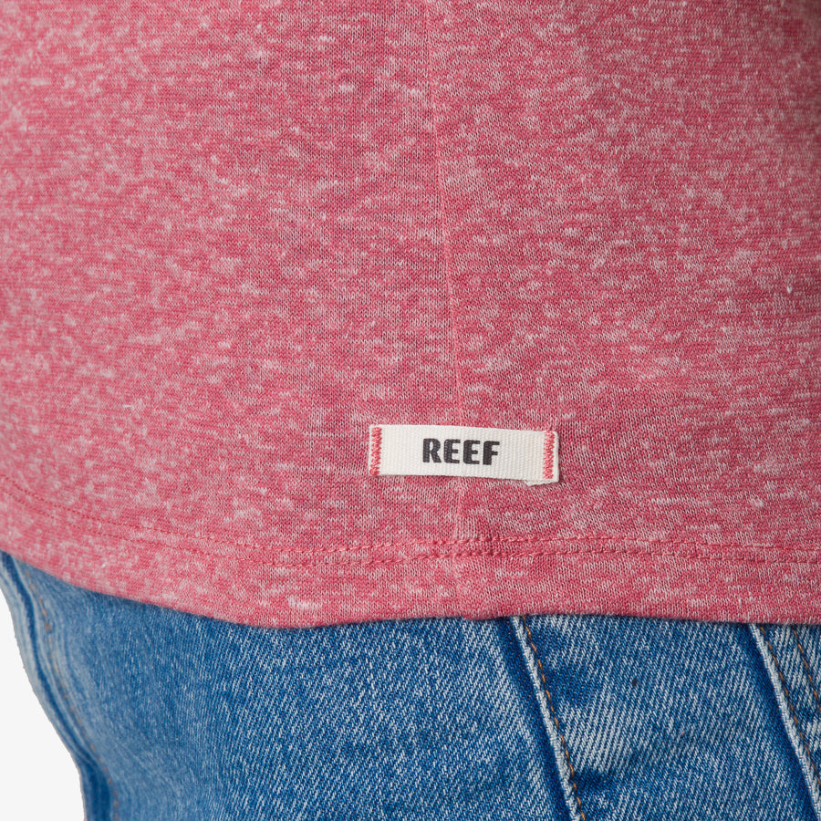 Close-up of the bottom hem of the mauve Saylor Fitted Tee showing REEF branding, paired with blue denim.