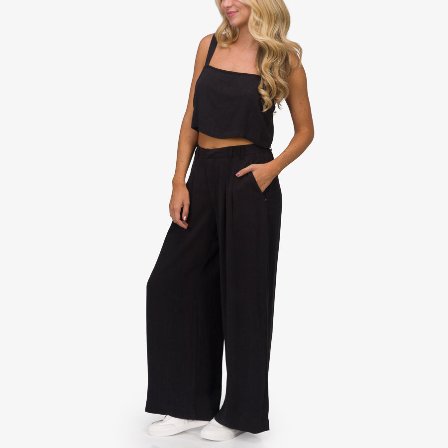 Woman wearing Tori Linen Tank in black front view paired with wide-leg pants and white shoes for beach comfort style