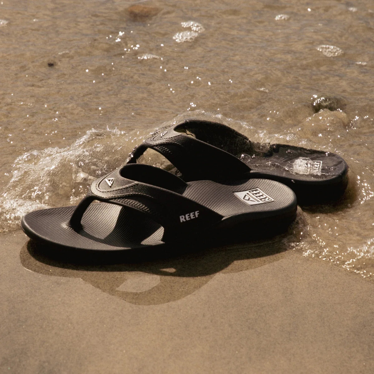 Pair of Fanning H2O men's sandals facing left on beach sand with water-friendly, cushioned footbeds and arch support.